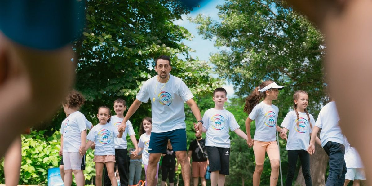 Children and an instructor playing together in a sunny park, holding hands and enjoying outdoor activities.