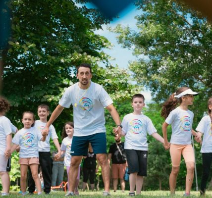 Children and an instructor playing together in a sunny park, holding hands and enjoying outdoor activities.