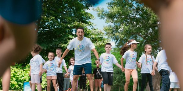 Children and an instructor playing together in a sunny park, holding hands and enjoying outdoor activities.