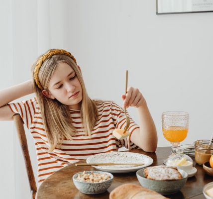 Teen girl in striped shirt at breakfast table with fruits, bread, and juice. Casual morning setting.