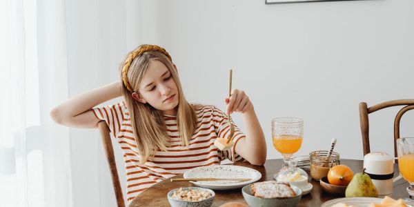 Teen girl in striped shirt at breakfast table with fruits, bread, and juice. Casual morning setting.