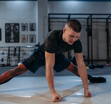 A male athlete stretches intensely in a dimly lit gym environment, preparing for training.