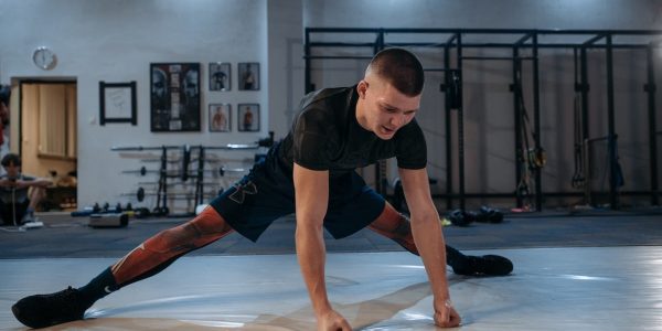 A male athlete stretches intensely in a dimly lit gym environment, preparing for training.